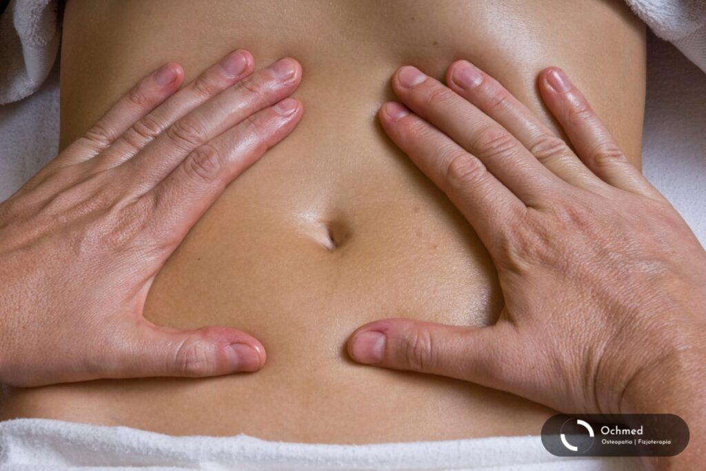 Dłonie masażysty na brzuchu pacjenta. Osteopatia wisceralna – na co pomaga masaż brzucha